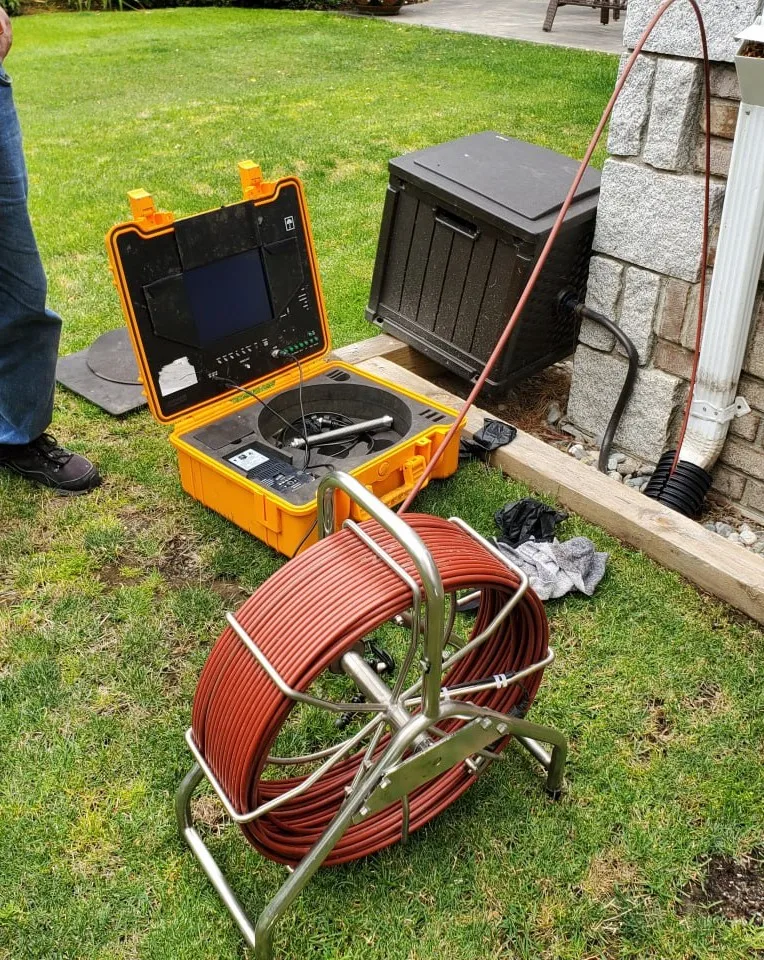 Drainstar Plumbing Inc. sewer camera monitor and reel set up on a lawn next to a house foundation