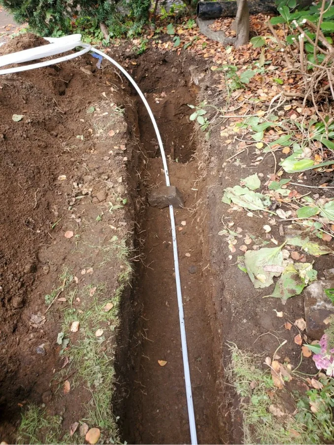 White PVC drainage pipe installed by Drainstar Plumbing Inc. in a trench running through a garden