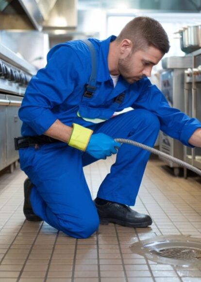 Plumber Unclogging Drain in Busy Restaurant Kitchen